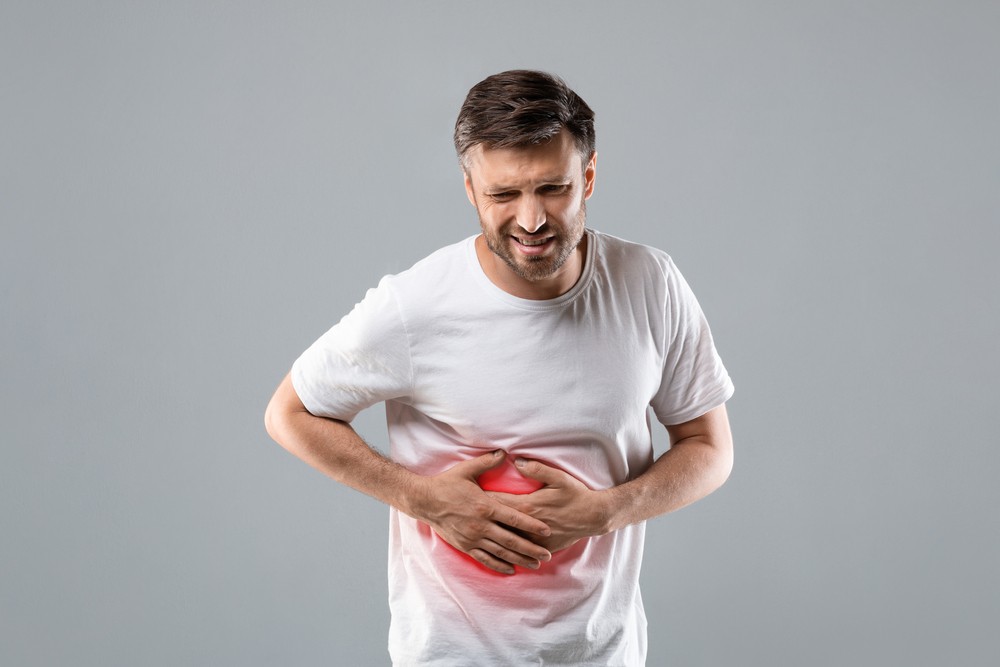 Middle-aged man holding his lightened with red right side, suffering from liver pain. shutterstock_1836036070